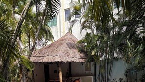 Une piscine dotée d’une structure à toit de chaume, entourée de palmiers et bordée d’un bâtiment à la façade blanche.