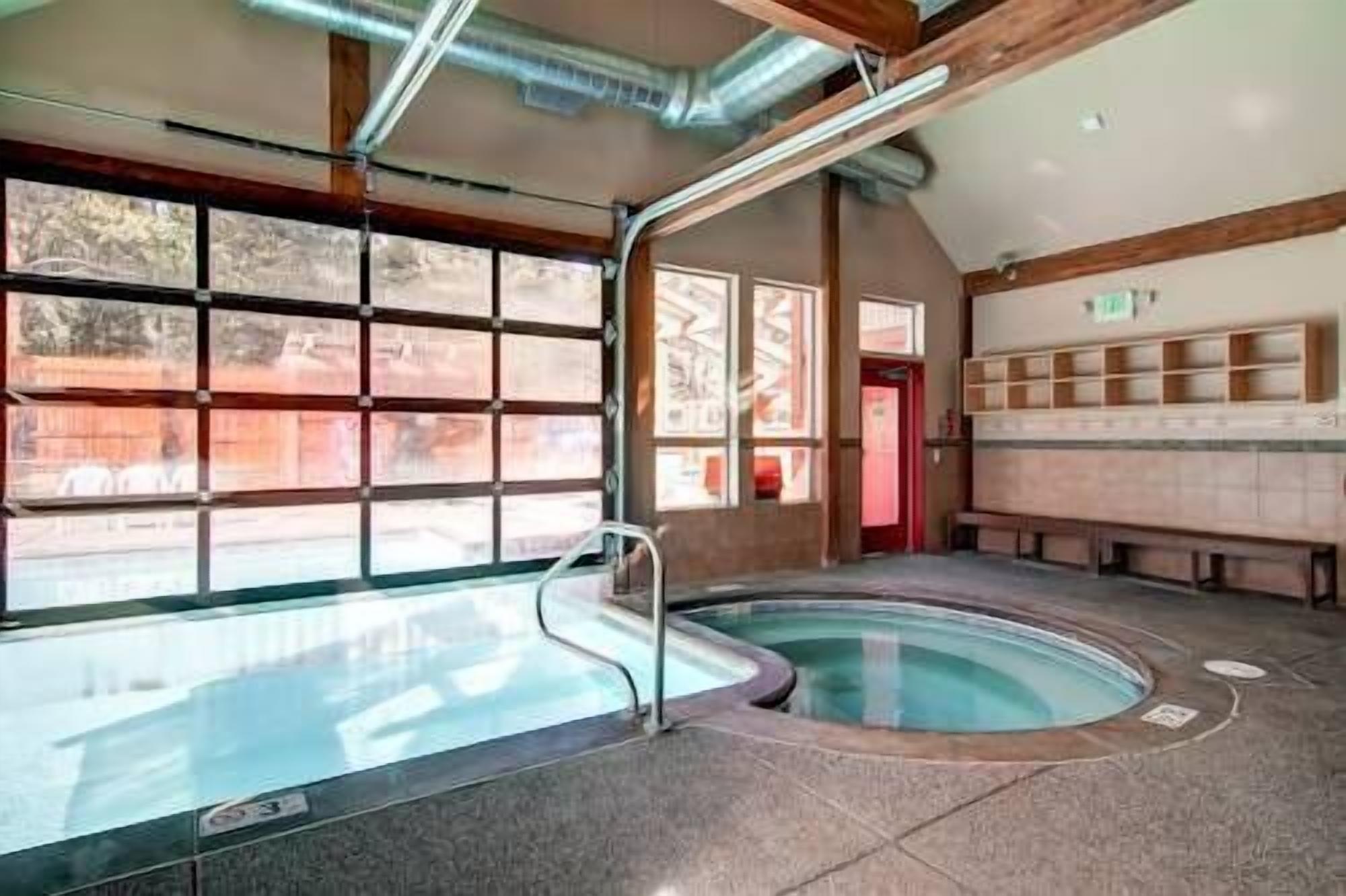 Une piscine dotée d’une structure en verre, de poutres en bois et d’un espace avec des bancs.