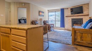A spacious living area with a large wooden bed, a fireplace, a TV mounted on the wall, and a kitchen area with a countertop and cabinets. - Best Location in Town! Ski-in/Ski-out on Peak 9! (Breckenridge)
