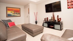 A living room with a brown leather sofa, a matching ottoman, a flat-screen TV mounted on the wall, and a decorative vase with red sticks. - Beautiful pool great location near to the beach. Special Prices for Nov and Dec! (Sarasota)