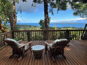 Une terrasse en bois avec deux chaises et une petite table, offrant une vue sur un paysage boisé et un plan d’eau.