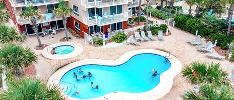 A multi-story hotel with a central swimming pool surrounded by lounge chairs and palm trees.