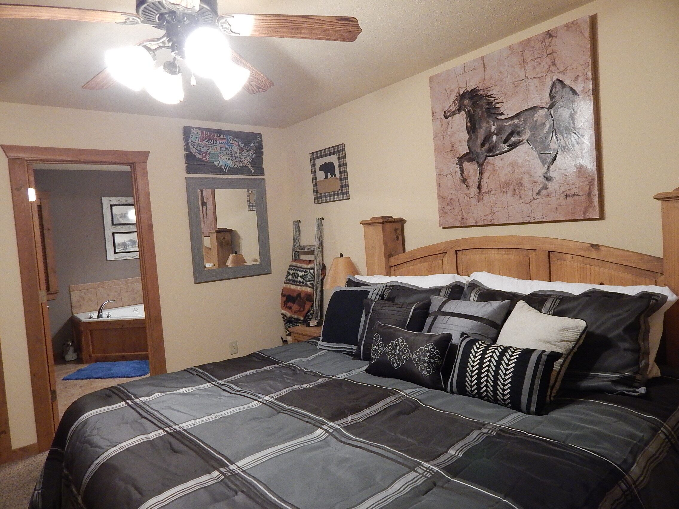 Un dormitorio con cama, ventilador de techo, un cuadro de un caballo, espejo y cómoda.