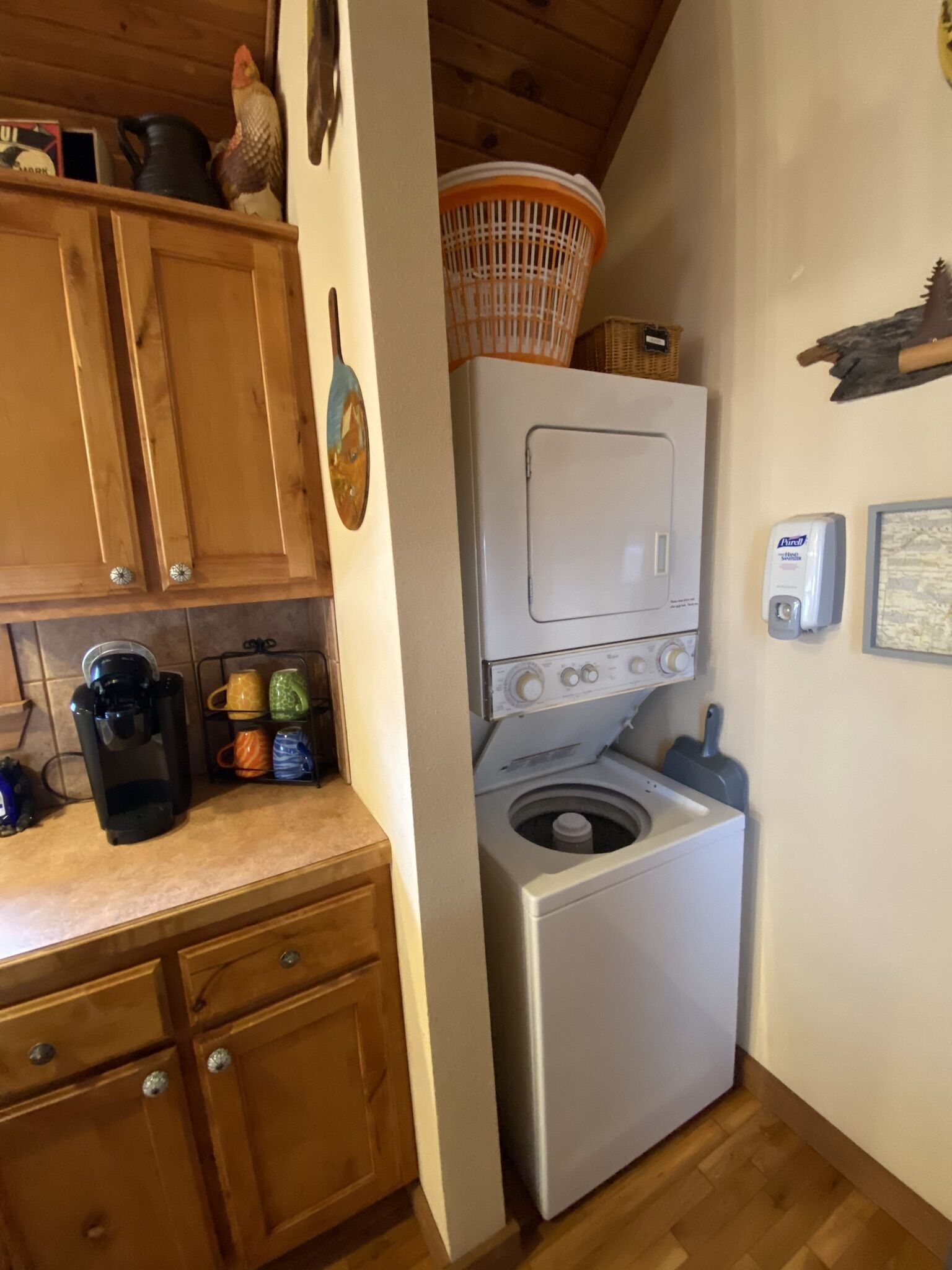 A compact kitchen with wooden cabinets, a coffee maker, a washing machine, and a basket on the counter.