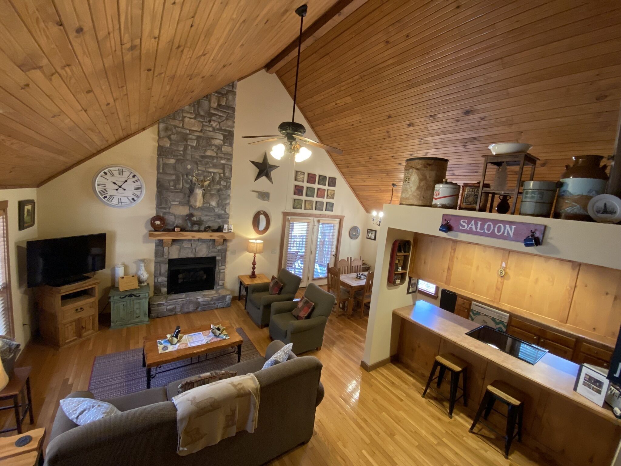 A cozy cabin interior with a stone fireplace, wooden ceiling, and a kitchen area labeled 'SALOON'.