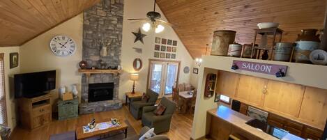 A cozy cabin interior with a stone fireplace, wooden ceiling, and a kitchen area labeled 'SALOON'.