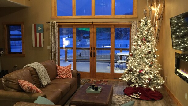 A cozy living room with a large window, a Christmas tree, and a fireplace.