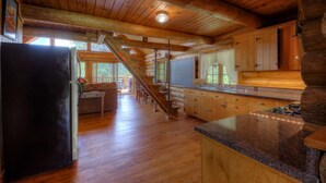 A log cabin interior with a kitchen, dining area, and a staircase leading to a loft.