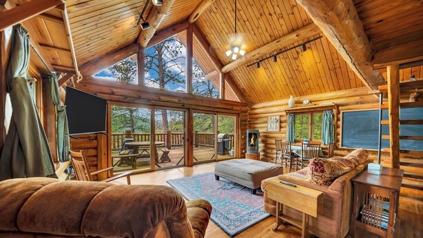 A cozy log cabin interior with a large open living area, wooden furniture, and a fireplace.