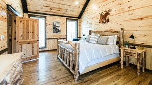 Un dormitorio de cabaña de madera con una cama, una mesita de noche, un aparador y una ventana.