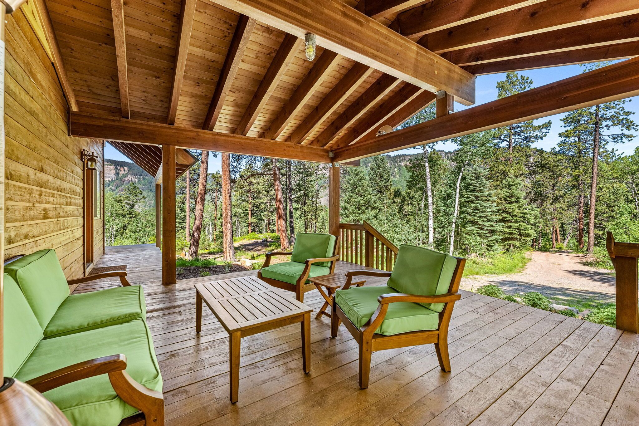 Une terrasse en bois avec des chaises rembourrées vertes et une table, donnant sur une zone boisée.