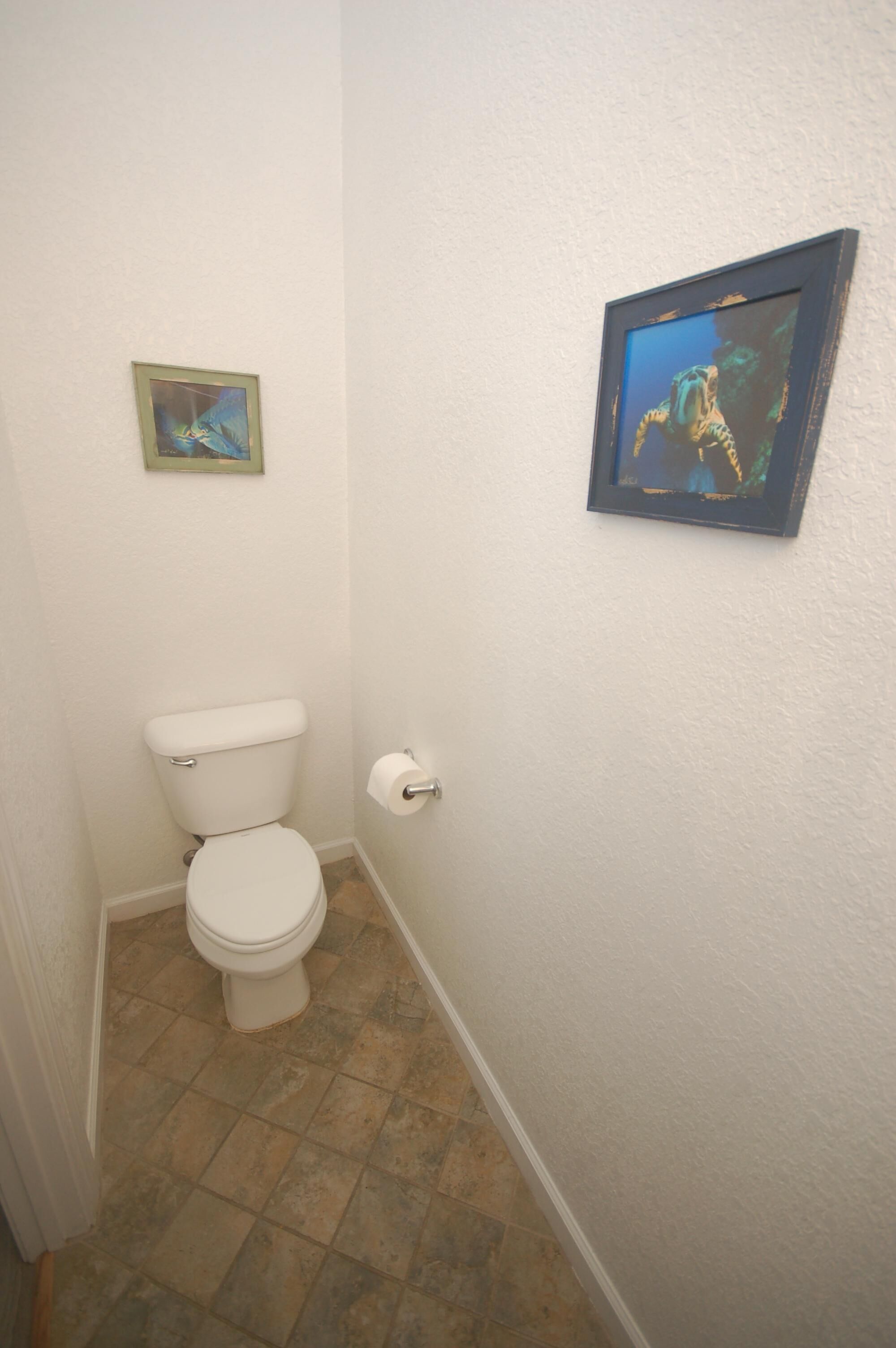 Een kleine badkamer met een toilet, een rol toiletpapier en twee foto's in lijsten aan de muur.