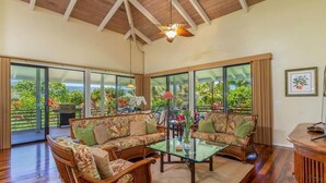 A spacious living area with a wooden ceiling, large sliding glass doors, and a view of lush greenery.