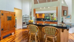 A spacious kitchen with a large island, wooden cabinets, and a dining area with wicker chairs.
