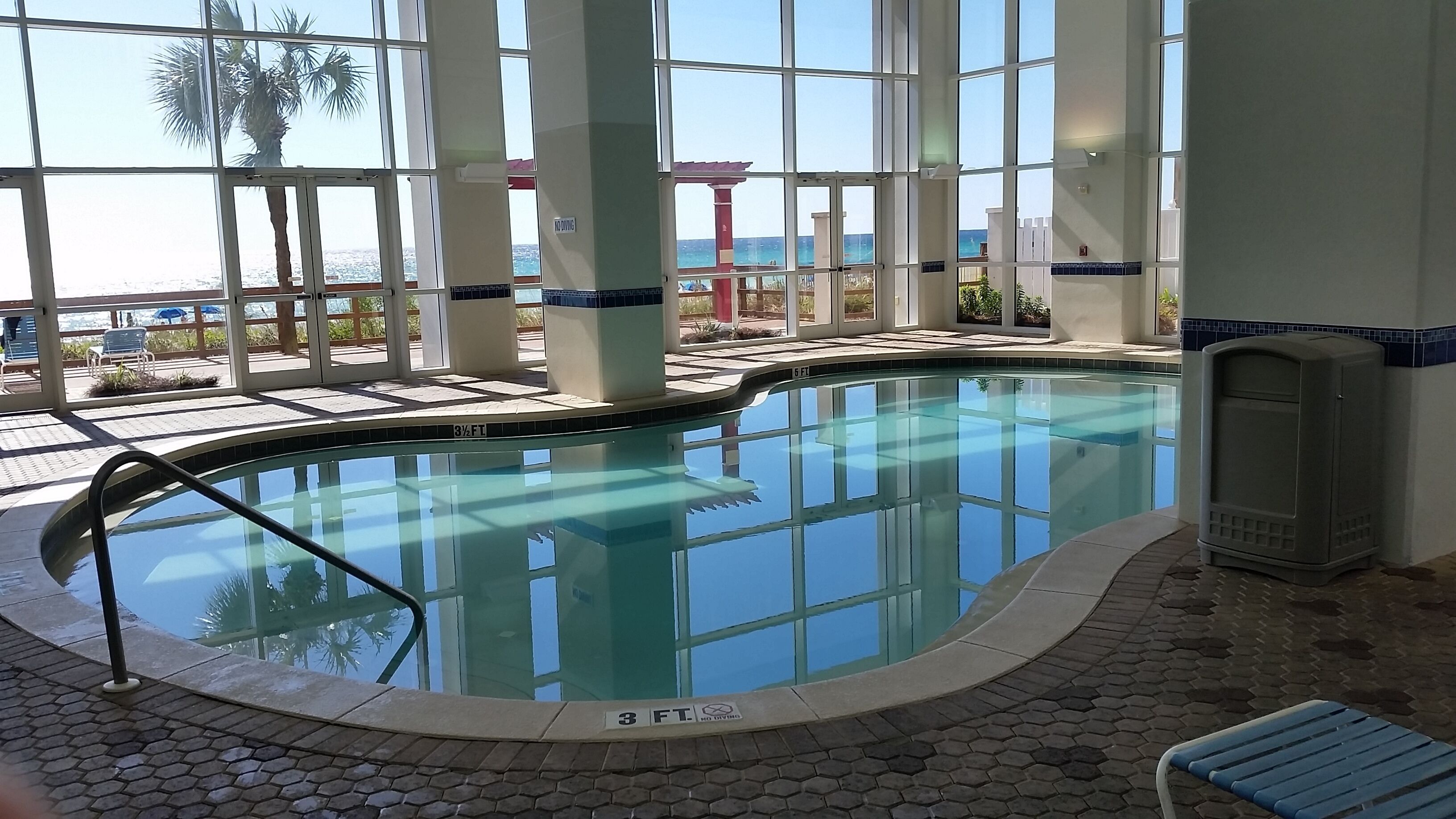 An indoor swimming pool with clear glass walls, a tiled floor, and a view of the ocean.