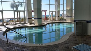 An indoor swimming pool with clear glass walls, a tiled floor, and a view of the ocean. - GREAT VIEW, FRIENDLY PRICES! (Panama City Beach)