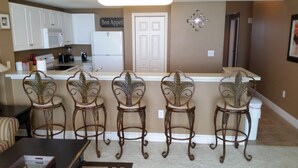 A kitchen with white cabinets, a microwave, and a refrigerator. There are four bar stools with leaf designs. A sign on the wall reads "Bon Appetit." - GREAT VIEW, FRIENDLY PRICES! (Panama City Beach)