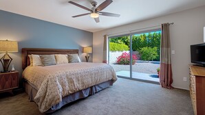 Un dormitorio con cama, ventilador de techo y vista a un jardín a través de una puerta corrediza de vidrio.