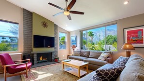 Una sala de estar moderna con chimenea, ventanas grandes y un ventilador de techo.