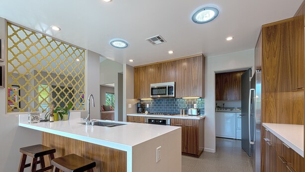Una cocina moderna con armarios de madera, una isla central con taburetes, microondas y refrigerador.