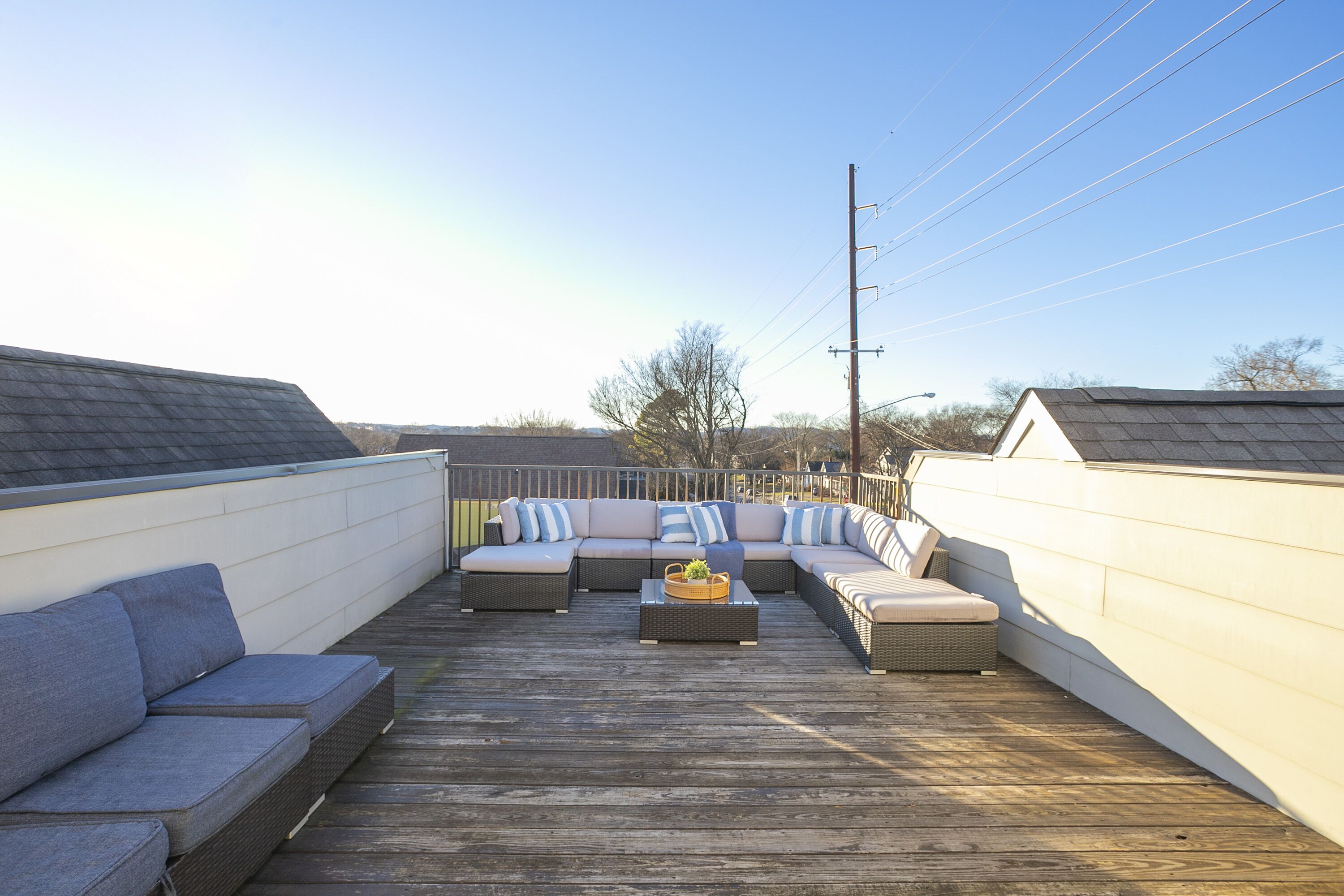 A wooden deck with a sectional sofa and a small table, surrounded by a white wall and a fence.