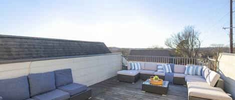 A rooftop patio with a sectional sofa, a small table, and a wicker chair.