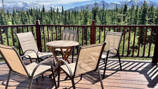 A wooden deck with a table and chairs, overlooking a forest and mountains. - 5 Star Denali Park Spacious Family Home (Healy)