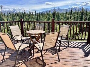 Una terraza de madera con una mesa y sillas, con vistas a un bosque y montañas.