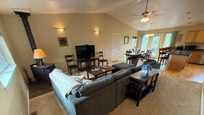 A spacious living room with a large gray sectional sofa, a dining area with wooden chairs, and a kitchen with wooden cabinets. - 5 Star Denali Park Spacious Family Home (Healy)