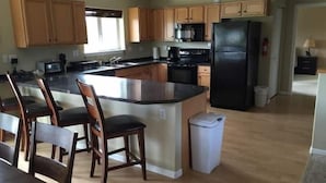 A modern kitchen with wooden cabinets, a black refrigerator, and a central island with chairs. - 5 Star Denali Park Spacious Family Home (Healy)