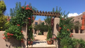 Un sentiero conduce a un edificio con una pergola in legno decorata da fiori rossi.