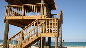 A wooden beach structure with a thatched roof, featuring multiple levels and a staircase.