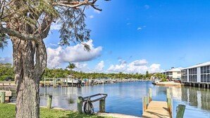 A marina with docked boats, a wooden dock, and a grassy area with a tree.