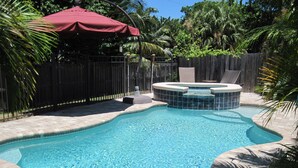 A swimming pool with a hot tub, surrounded by a wooden fence and palm trees.