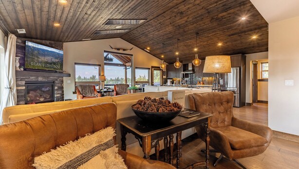 A spacious living area with a wooden ceiling, a large flat-screen TV, a fireplace, and a view of the outdoors. - 20 acres private ranch with Mountain View’s  (Bend)
