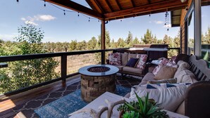 A covered outdoor seating area with a stone fire pit, a sofa, and a dining table. - 20 acres private ranch with Mountain View’s  (Bend)