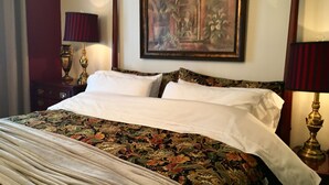 A bed with a floral bedspread, two white pillows, and a headboard. There are two bedside tables with lamps and a framed painting on the wall.