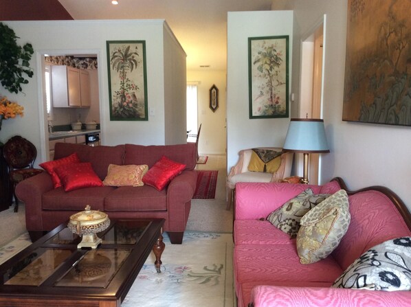 A living room with a red sofa, a glass coffee table, and a pink sofa with patterned cushions.