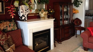 A living room with a fireplace, a red sofa, a wooden cabinet, and a dining area with a red chair.