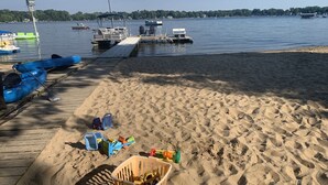 Een zandstrand met kajaks, een paddleboard en strandgerei. Bootjes liggen afgemeerd op de achtergrond.