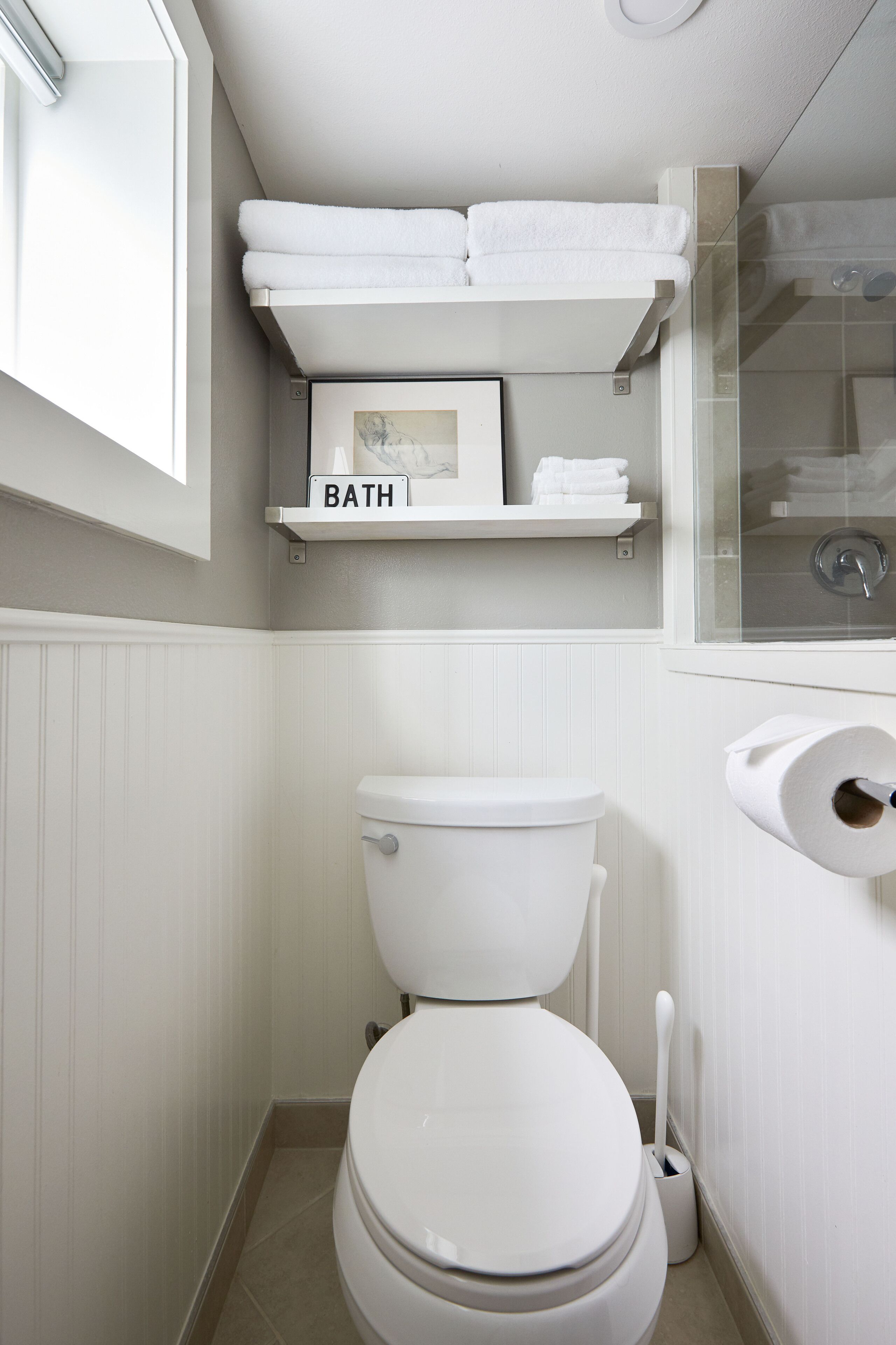 A bathroom with a toilet, a shelf labeled "BATH," and a roll of toilet paper.