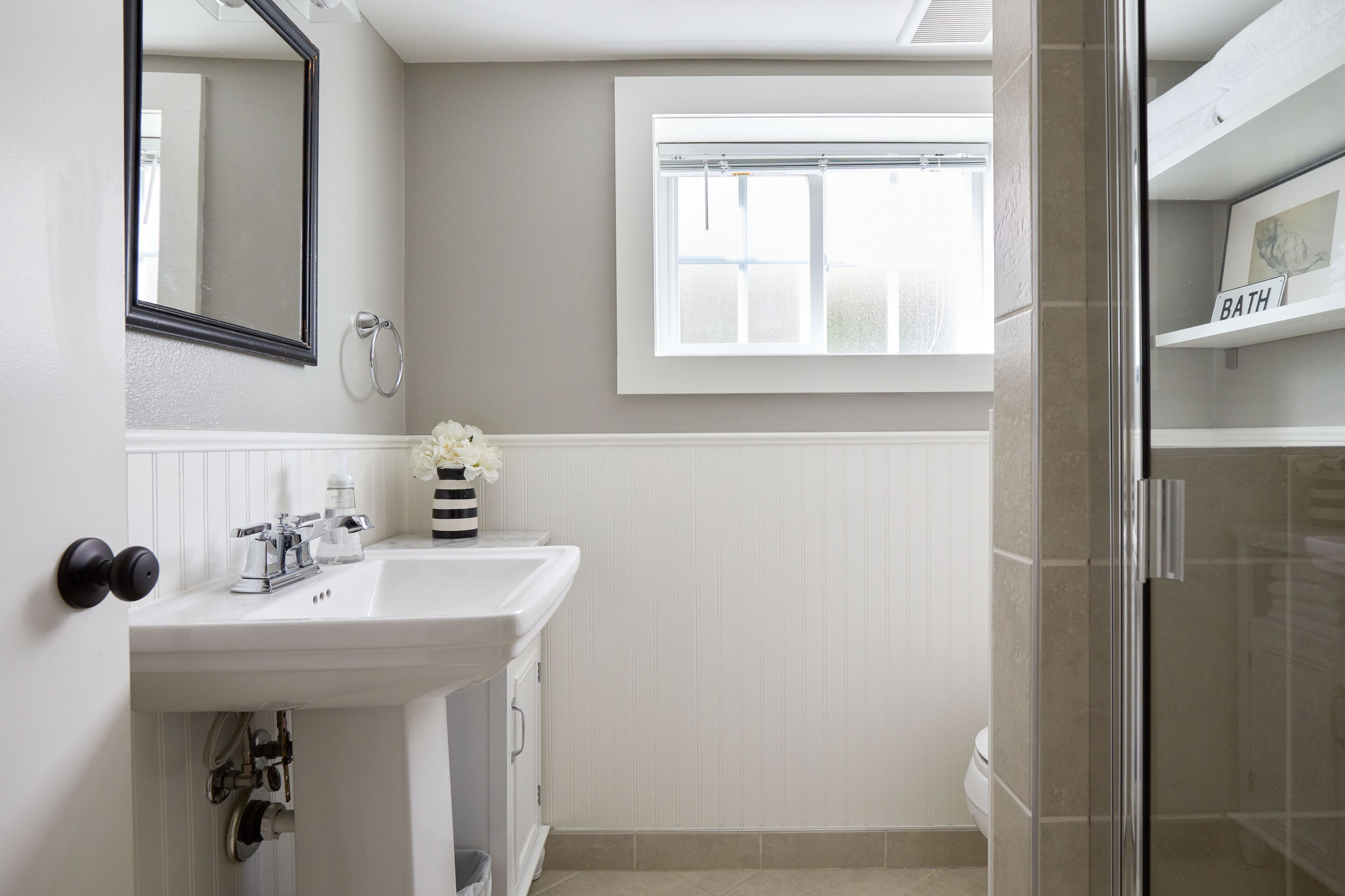A bathroom with a white sink, a mirror, a window, and a shower area.