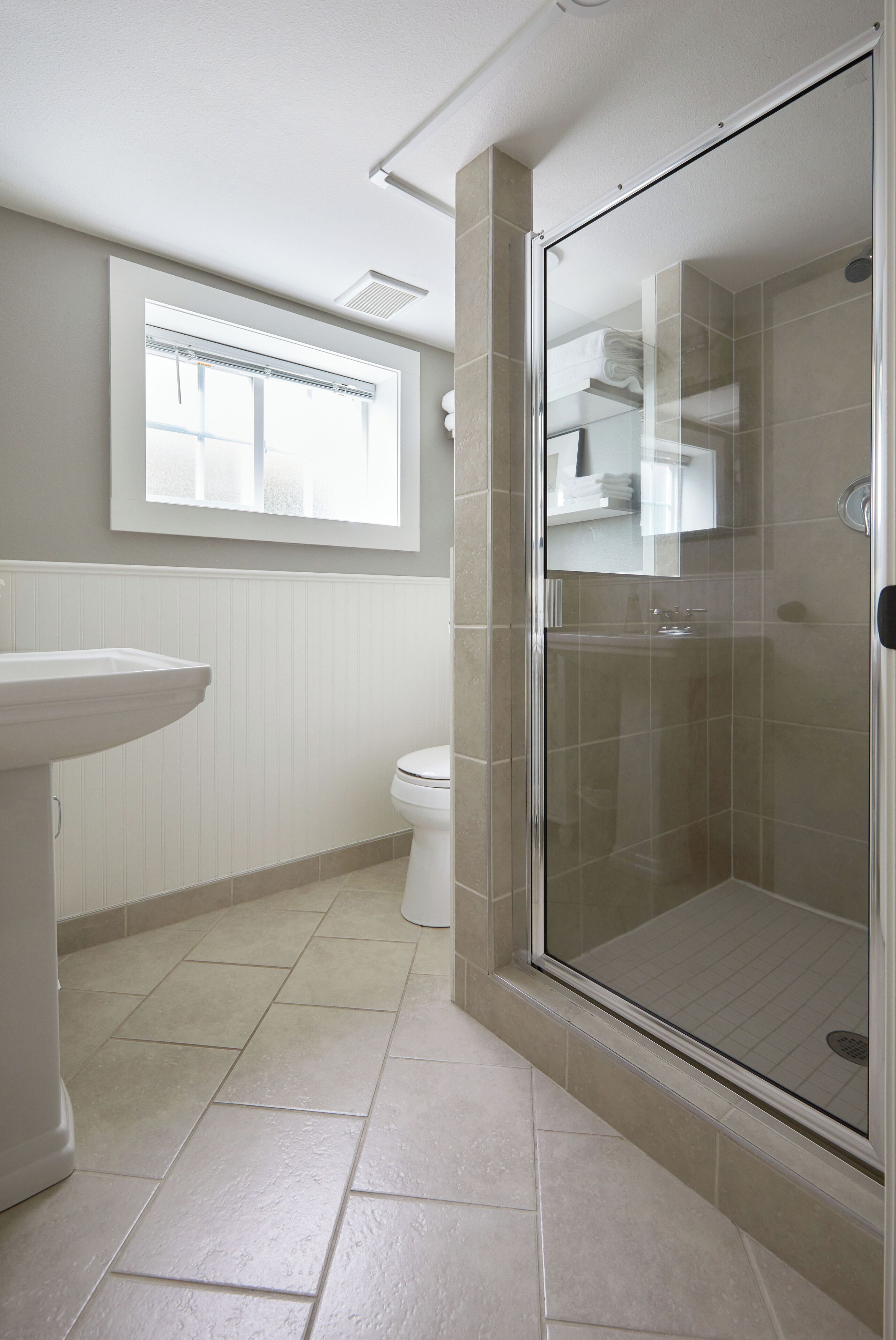 A bathroom with a glass-enclosed shower, a pedestal sink, and a toilet.