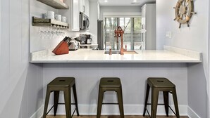 Une cuisine moderne avec des meubles blancs, un îlot central doté de tabourets et une décoration en forme de barre de navire sur le mur.