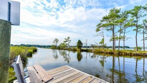 Une jetée en bois s’étendant dans une rivière paisible, avec des arbres et un ciel dégagé en arrière-plan.