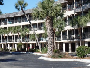 A multi-story hotel with balconies, palm trees, and a parking lot.