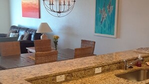 Uma cozinha com bancadas de granito, pia de aço inoxidável, armários de madeira e um lustre moderno.