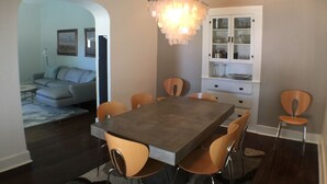 A dining area with a rectangular table, six chairs, a chandelier, a cabinet with dishes, and a sofa in the background. - Renovated Adobe One Block From Marfa Courthouse Across From The Hotel Paisano (Marfa)