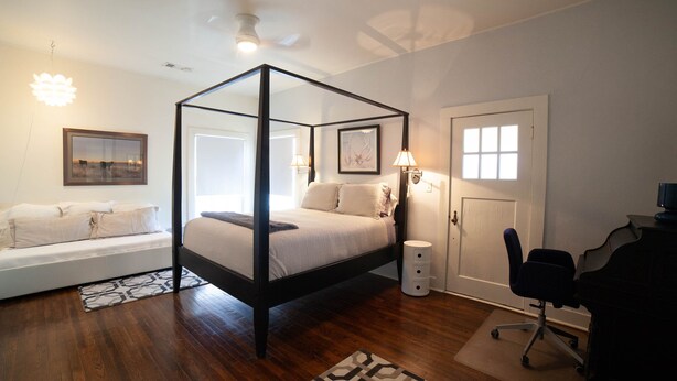 A bedroom with a four-poster bed, a desk with a chair, a sofa, and a door with a window. - Renovated Adobe One Block From Marfa Courthouse Across From The Hotel Paisano (Marfa)
