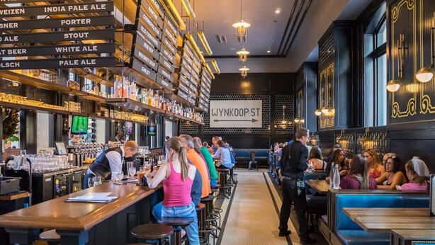 A bar area with a variety of liquor bottles, a bar counter, stools, and a seating area with tables and chairs. - Rock House in Berkeley neighborhood of Denver (Denver)
